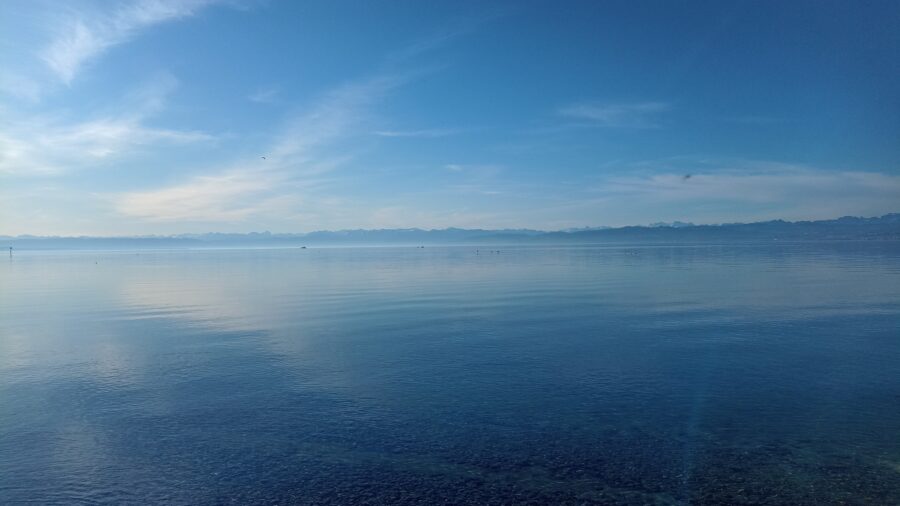 Spiegelglatter Bodensee in verschiedenen Blautönen mit Bergpanorama