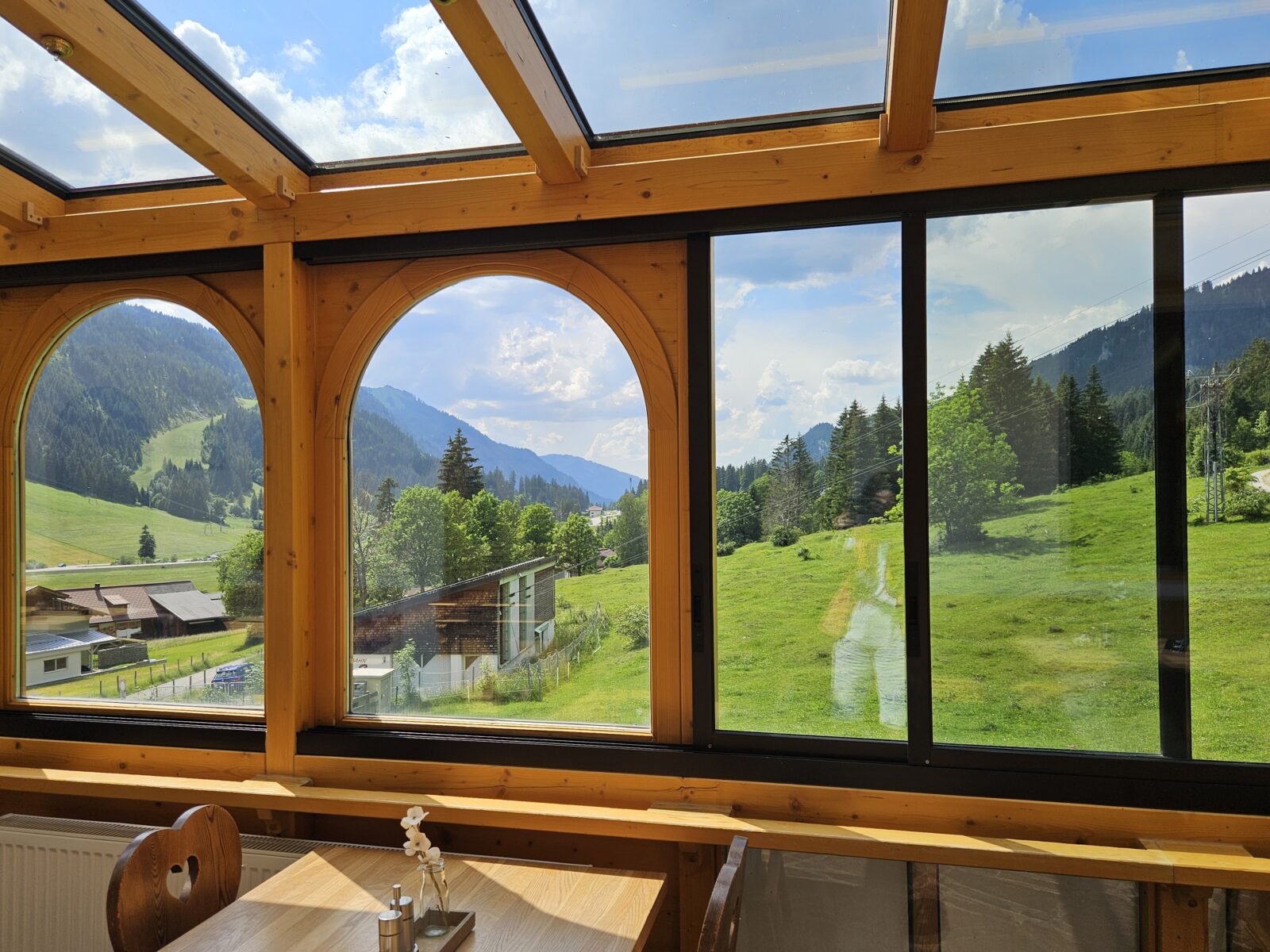 Wintergarten des Hotels Berghof in Nesselwängle mit Blick auf grüne Wiesen und Berge