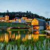 Außenansicht des beleuchteten Pfalzblick Wald Spa Resorts im Pfälzerwald mit Naturbadeteich und Sauna-Insel