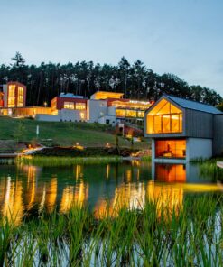 Außenansicht des beleuchteten Pfalzblick Wald Spa Resorts im Pfälzerwald mit Naturbadeteich und Sauna-Insel