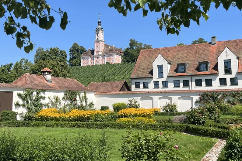 Blühender Garten von Schloss Maurach am Bodensee mit dem Wohngebäude und Schloss Birnau im Hintergrund